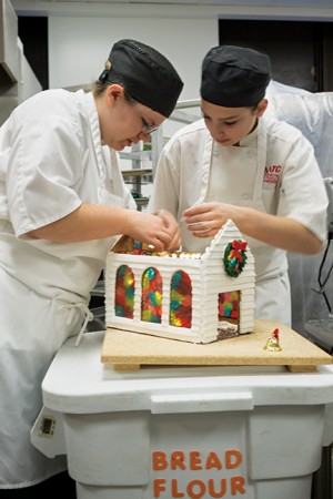 Abby Diedrich and Kelsey Combs, Baking and Pastry Arts program, attach lights to the inside of their gingerbread house for a little sparkle in their entry for the competition.