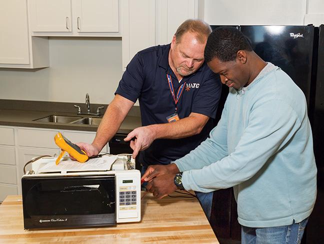 Jim Rehm, instructor for the Appliance Services program, shows Gilbert Jackson how to use a multimeter to troubleshoot a microwave oven.