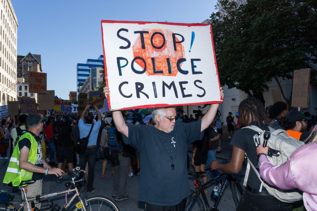 Brian Verdin, a member of Milwaukee Alliance Against Racist Political Repr.ession, holds a sign that reads "Stop Police Crimes"