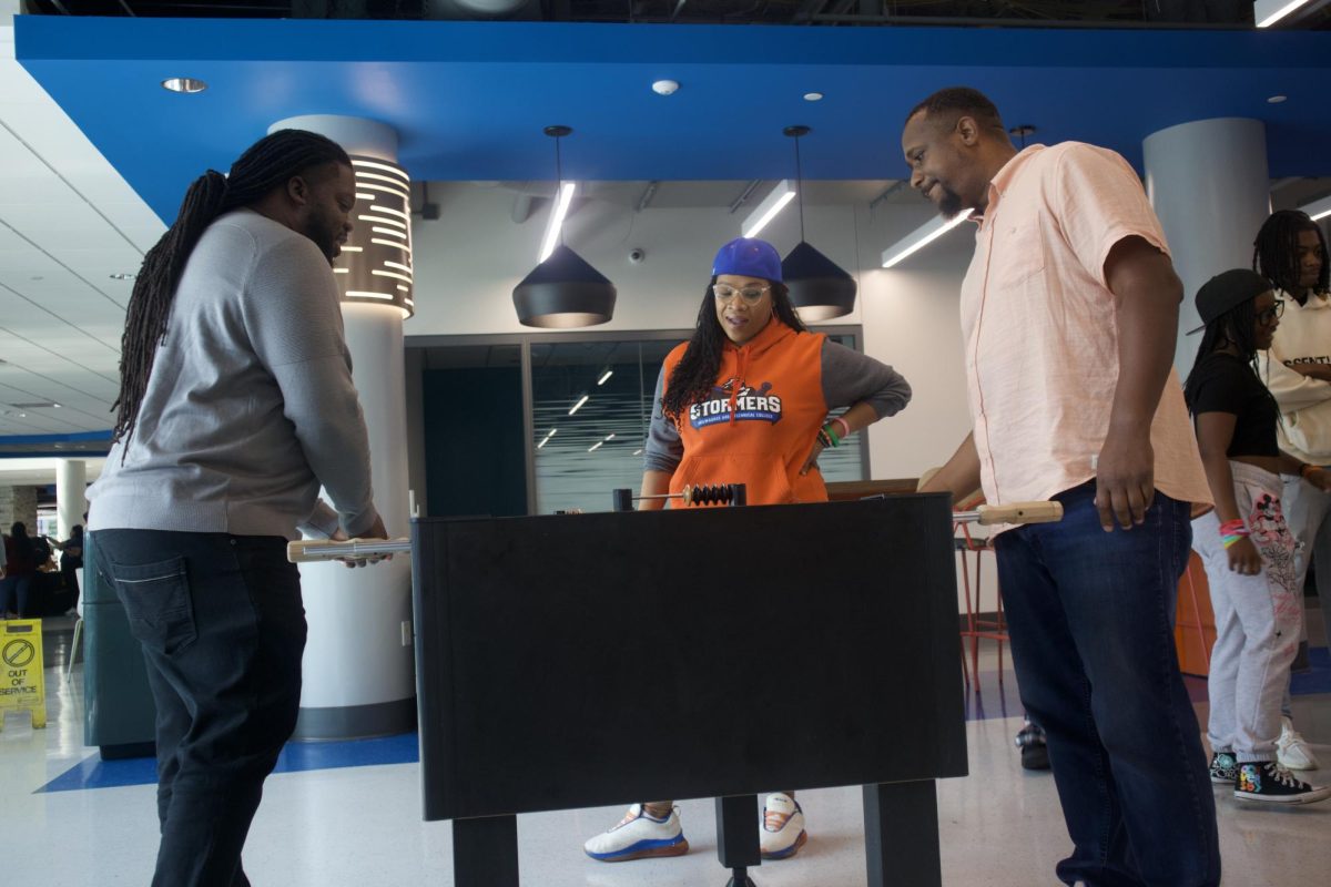 Dean of Student Experience Equan Burrows (L) enjoys playing foosball in the new 3rd floor Downtown Student Lounge as Student Life Coordinator Amanda Brooks watches. Burrows is playing against Will Johnson Coordinator of MOCI (Men of Color Initiative).