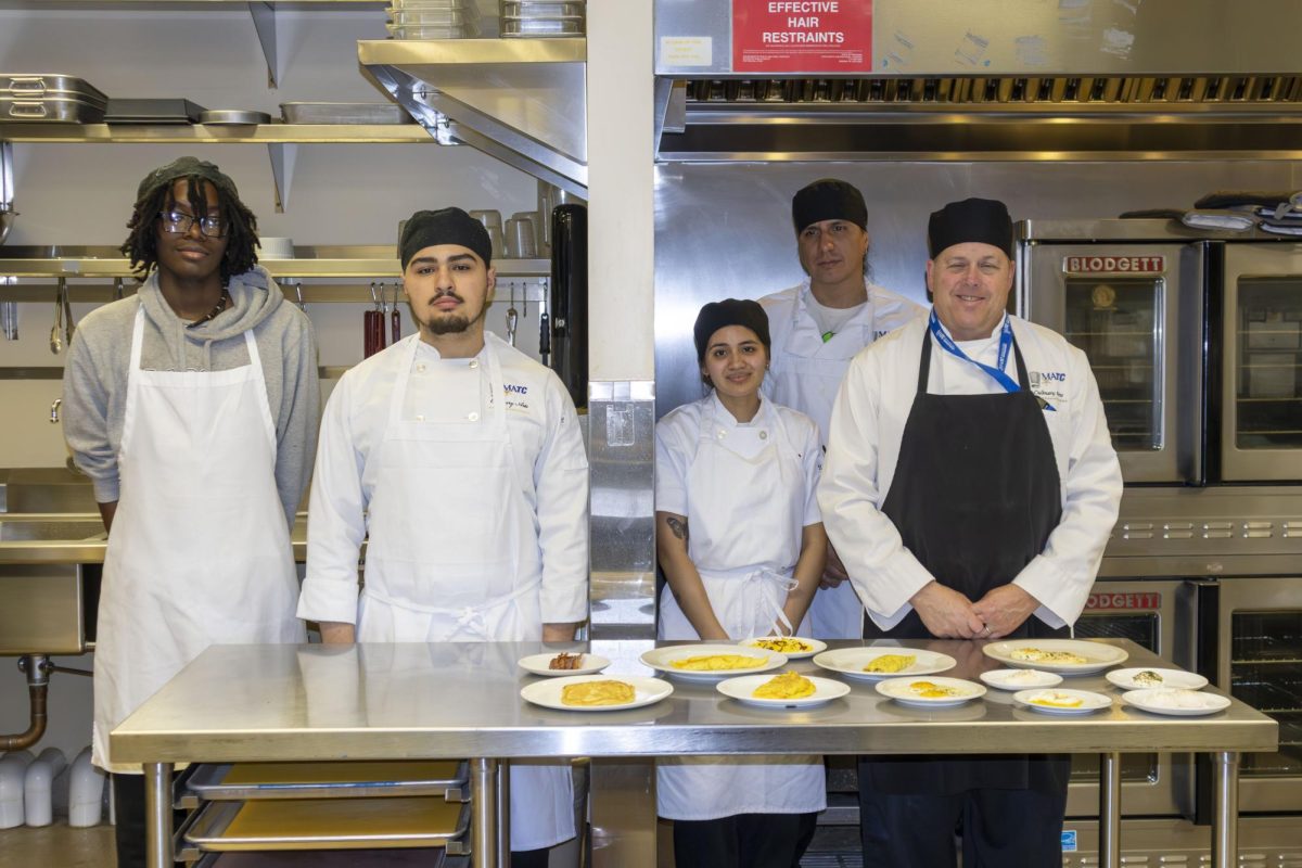 Culinary Fundamentals students pose with Chef Paul (right) in a kitchen on the 6th floor of the M Building at the Downtown Campus.