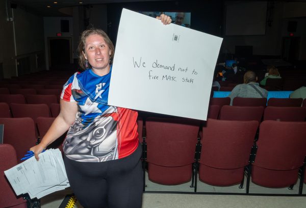 Former student worker in the Multicultural Affairs office, Monique Valentine, stands with protest signs in the Cooley Auditorium during the live stream of MATC’s Board Meeting on August 26, 2025. 